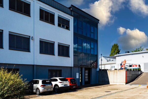 Bürogebäude mit blauer Fassade und Glasfront, davor parkende Autos